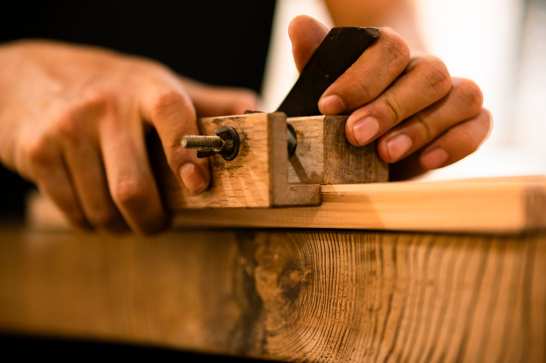 Hände führen einen Hobel über ein Holzbrett, traditionelle Holzbearbeitung.